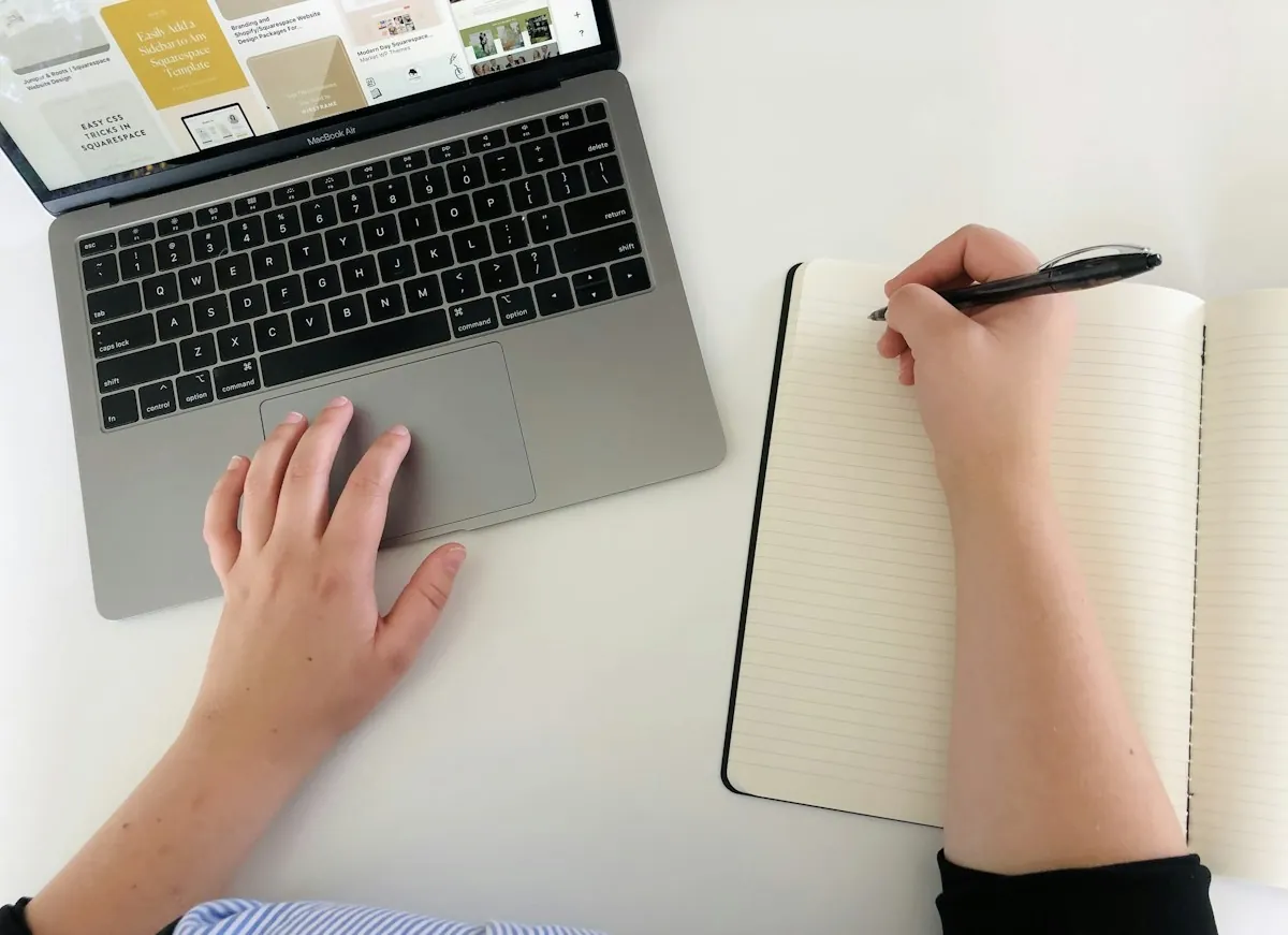 Des mains écrivent dans un carnet à côté d’un ordinateur portable